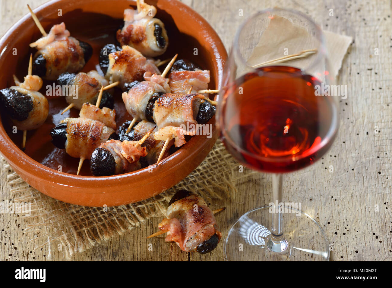 Deliziose tapas spagnole: fritto prugne avvolto in pancetta servita portoghese con il vino di porto Foto Stock