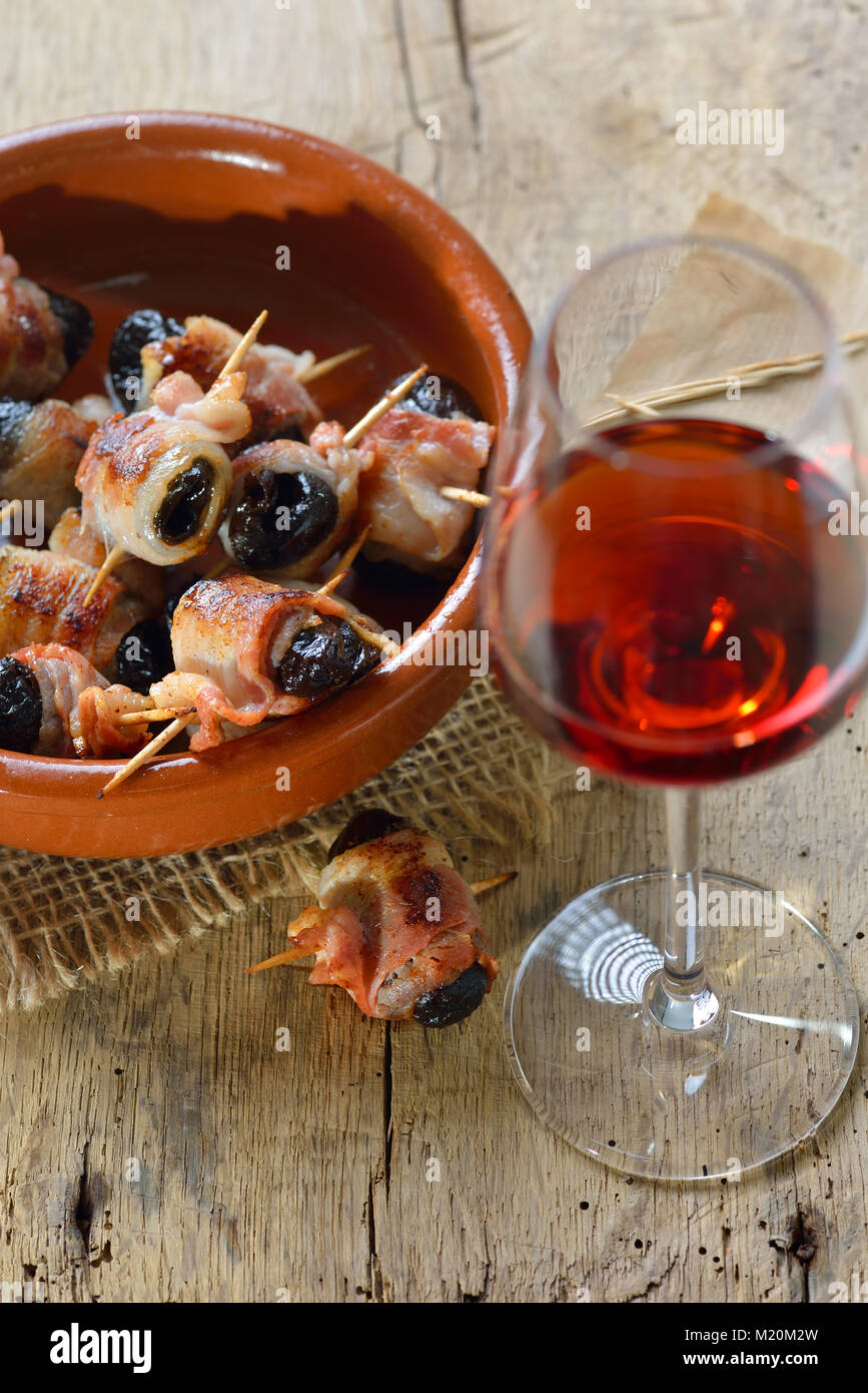 Deliziose tapas spagnole: fritto prugne avvolto in pancetta servita portoghese con il vino di porto Foto Stock