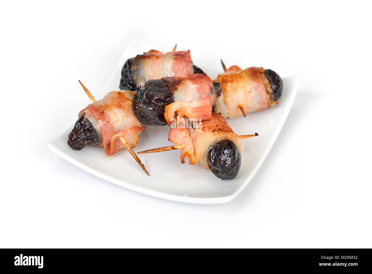 Deliziose tapas spagnole su sfondo bianco: fritto prugne avvolto in pancetta Foto Stock