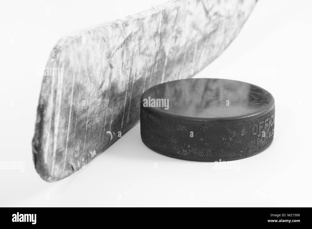 Primo piano di hockey su ghiaccio stick blade avvolto in rigata nastro bianco e un usato puck su sfondo bianco; immagine monocromatica Foto Stock