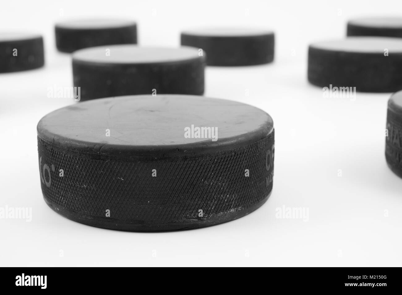 Usato ice hockey puck disposte casualmente su sfondo bianco; immagine monocromatica, angolo obliquo view Foto Stock