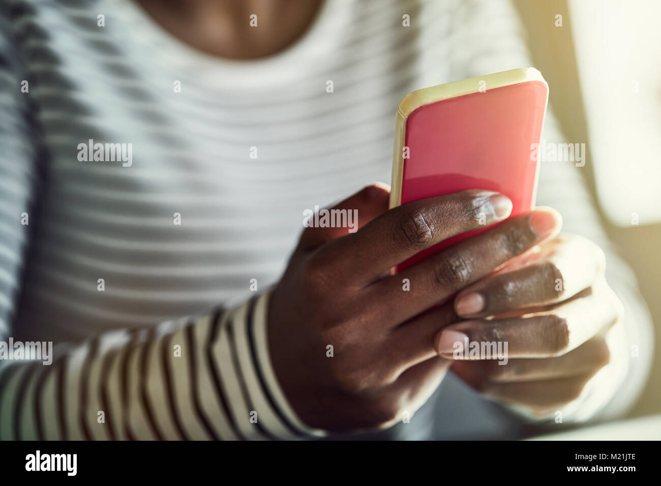 Primo piano di una giovane donna africana seduto da solo a un tavolo di lettura dei messaggi di testo sul suo cellulare Foto Stock