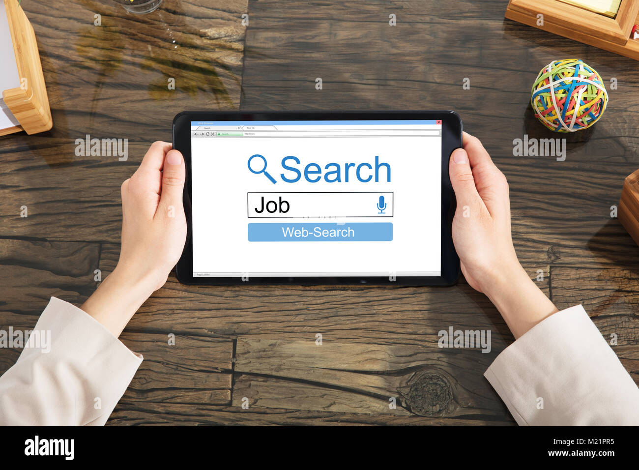 Close-up di una persona alla ricerca di lavoro online su tavoletta digitale sulla scrivania in legno Foto Stock