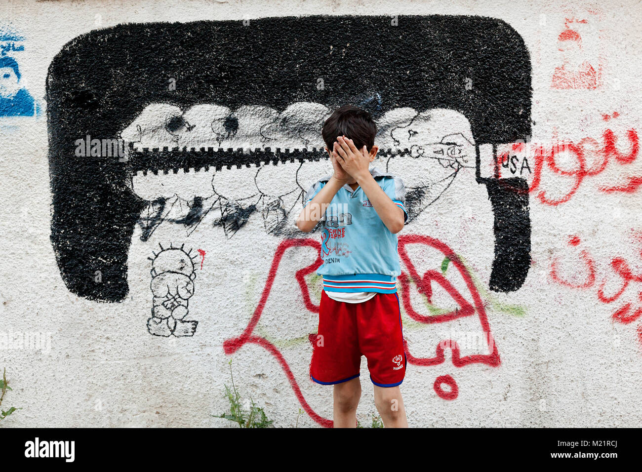 Betlemme, Palestina, Giugno 30, 2014: Boy in piedi sulla strada di un campo profughi nel centro di Betlemme. Graffiti sui muri di una parte di Pales Foto Stock