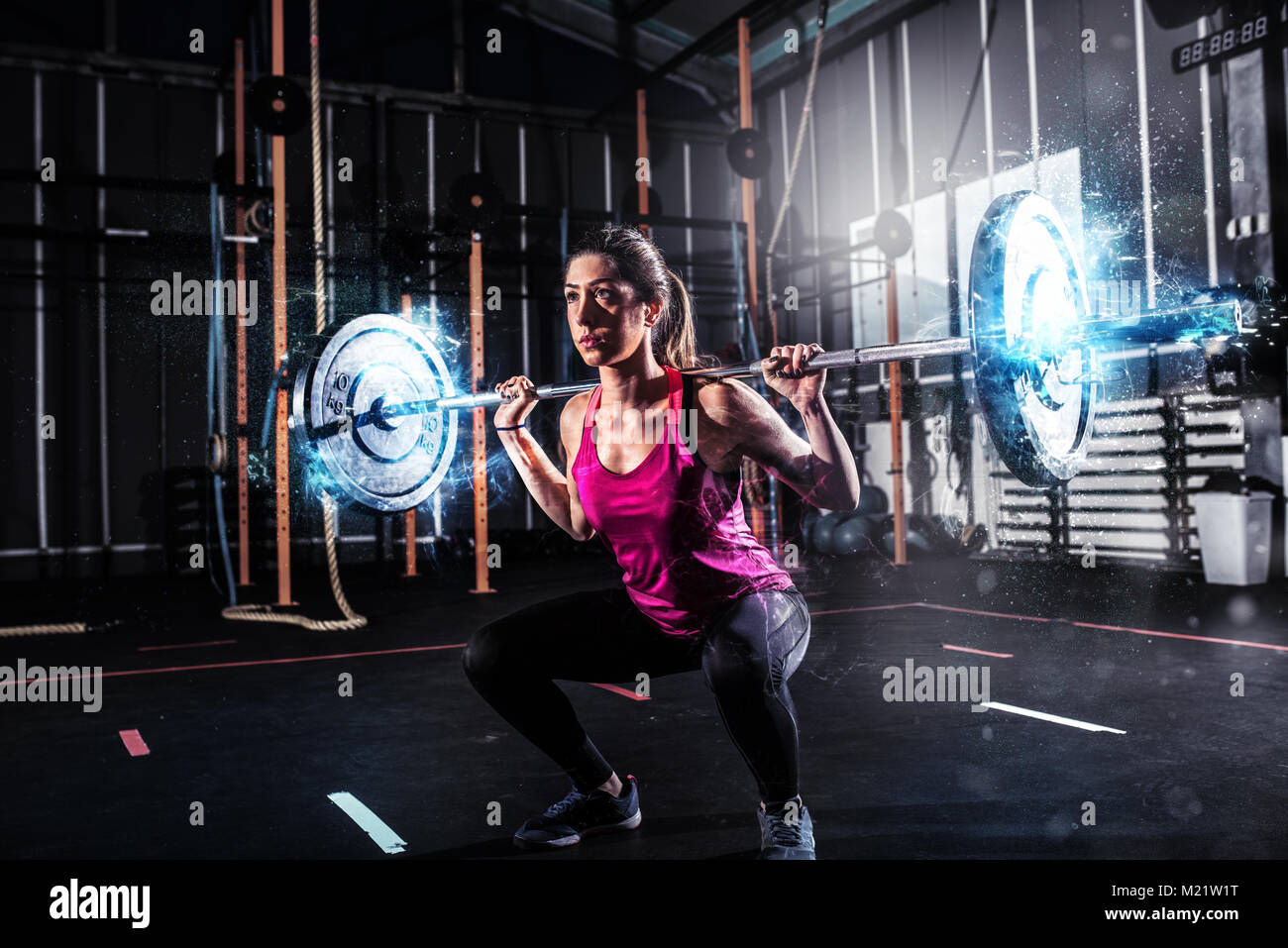 Athletic ragazza lavora presso la palestra con un barbell blu con effetti di energia Foto Stock