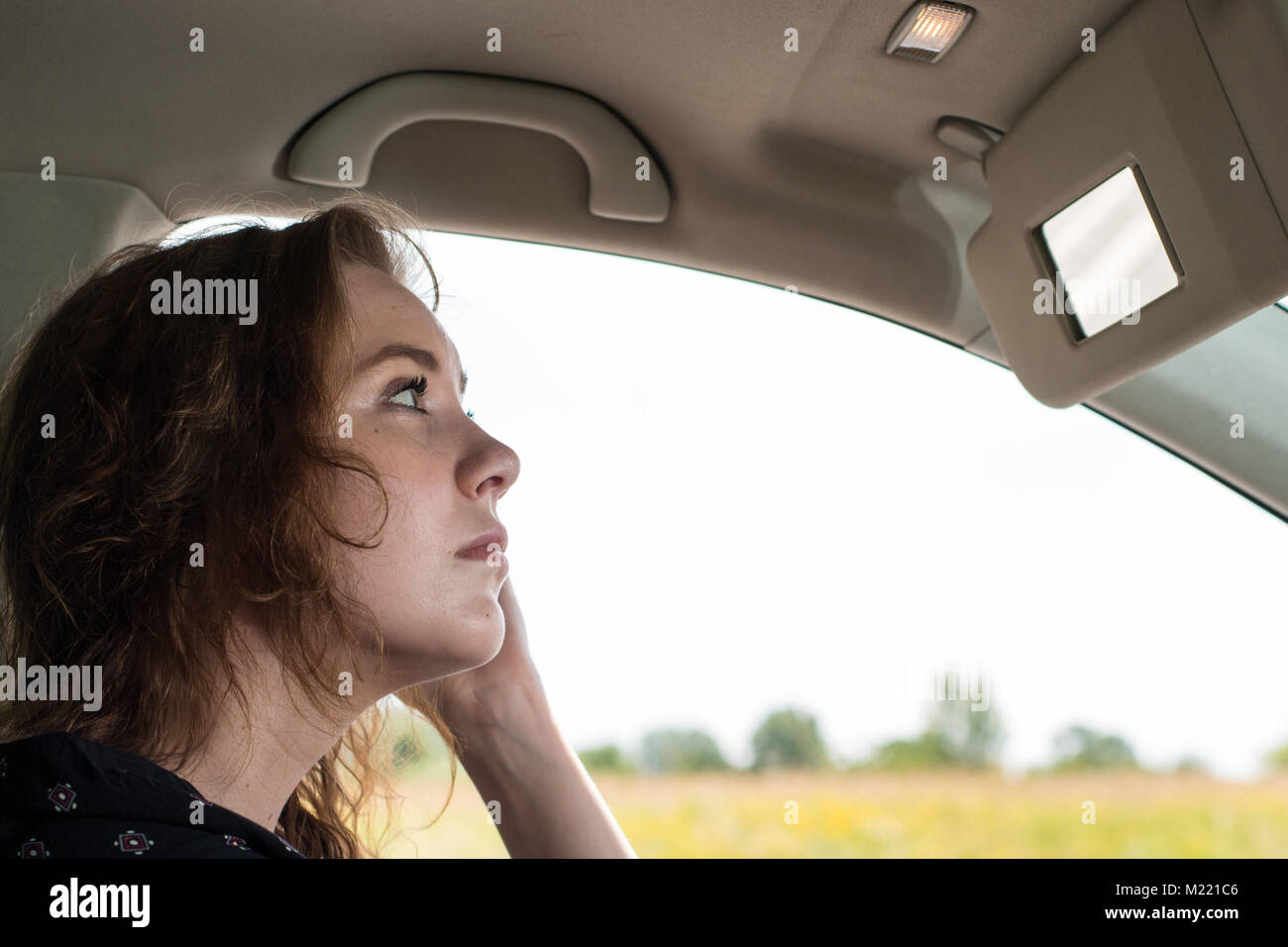 Una giovane donna aziona una vettura e raddrizza i suoi capelli durante la guida Foto Stock