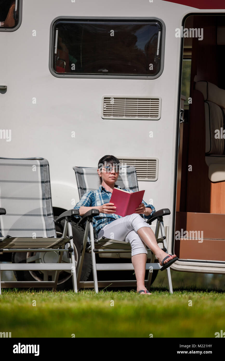 La donna si rilassa e legge un libro vicino al campeggio . Caravan auto vacanza. Vacanza per la famiglia in viaggio, viaggio vacanza in camper RV. Foto Stock