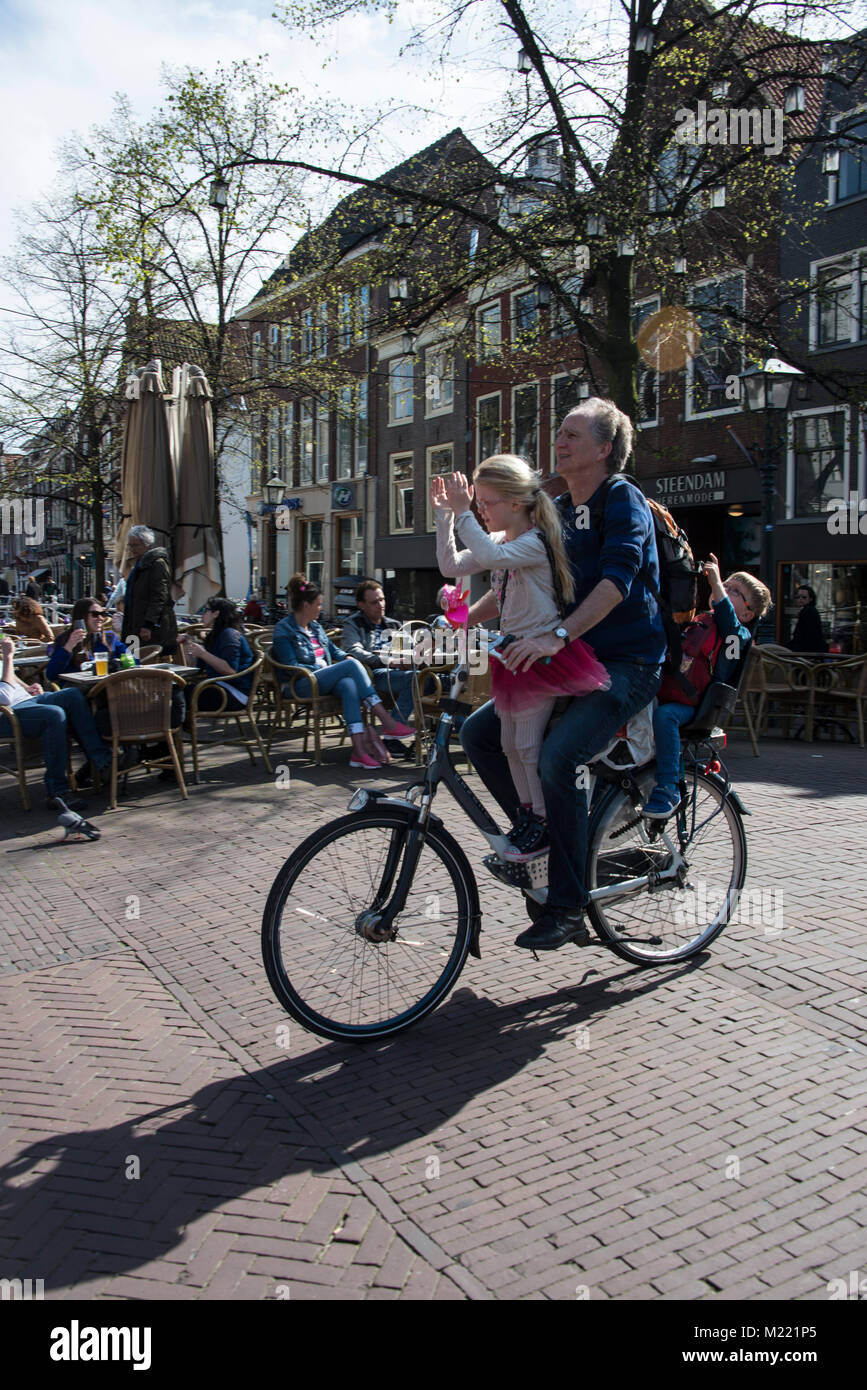 Un padre che porta due dei suoi giovani figli sulla sua bicicletta in una strada trafficata in Delft città vecchia, Olanda. Indossare dei caschi da bicicletta non è compuls Foto Stock