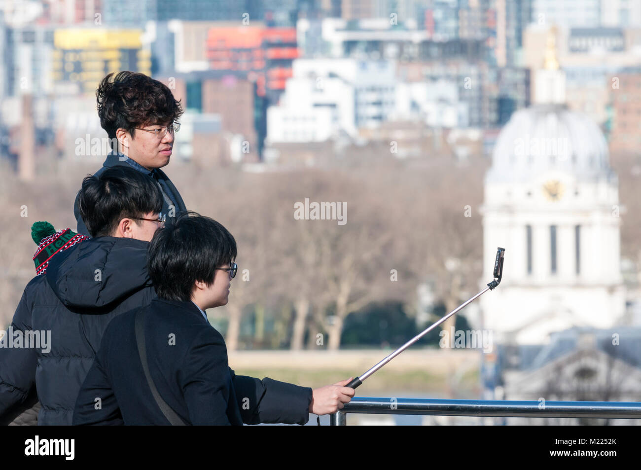 Turisti asiatici usando un bastone selfie a prendere un selfie a Greenwich davanti la vista sul fiume Tamigi Foto Stock