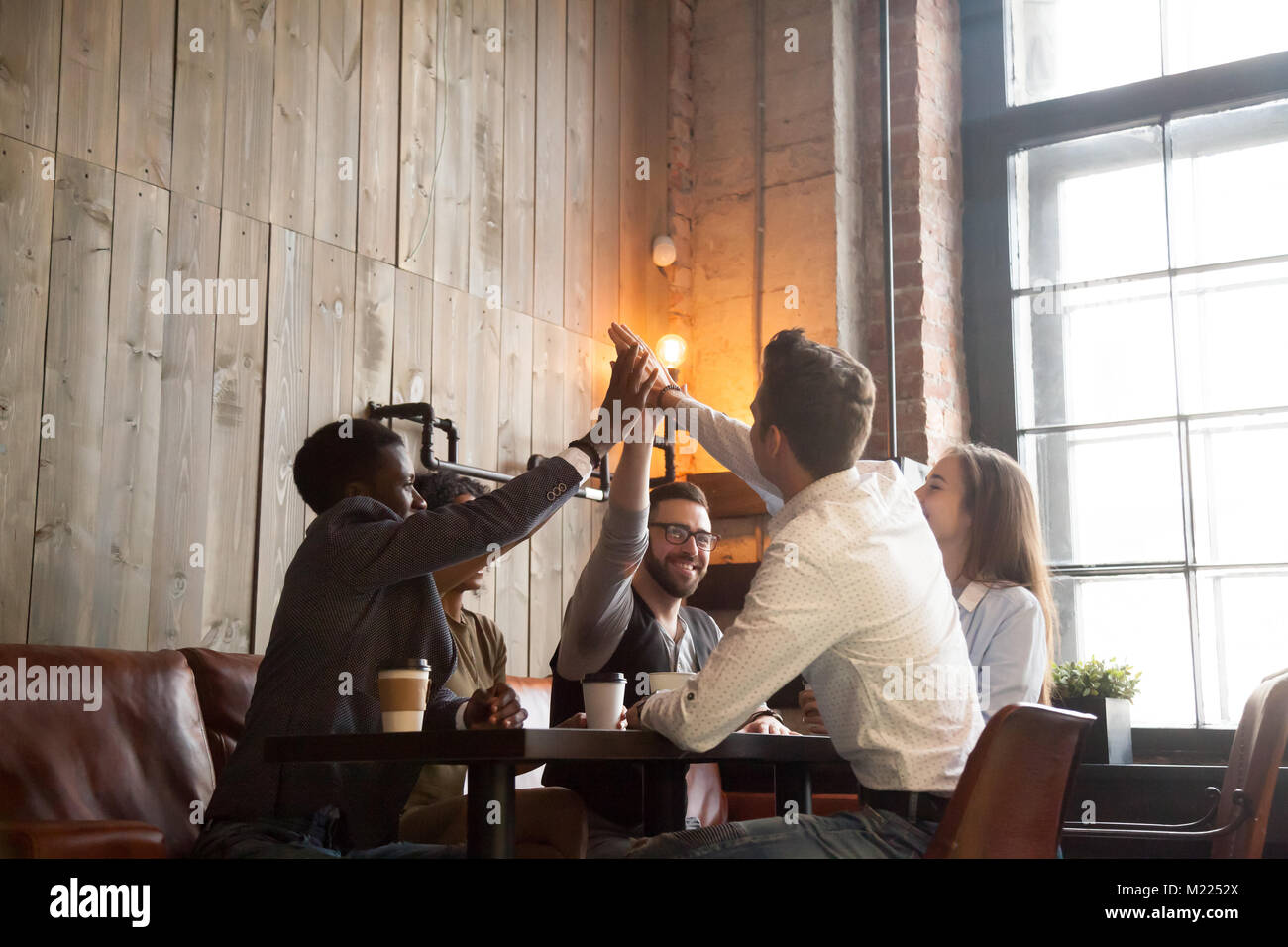 Multirazziale gruppo amici dando alta cinque seduti al tavolo del bar Foto Stock
