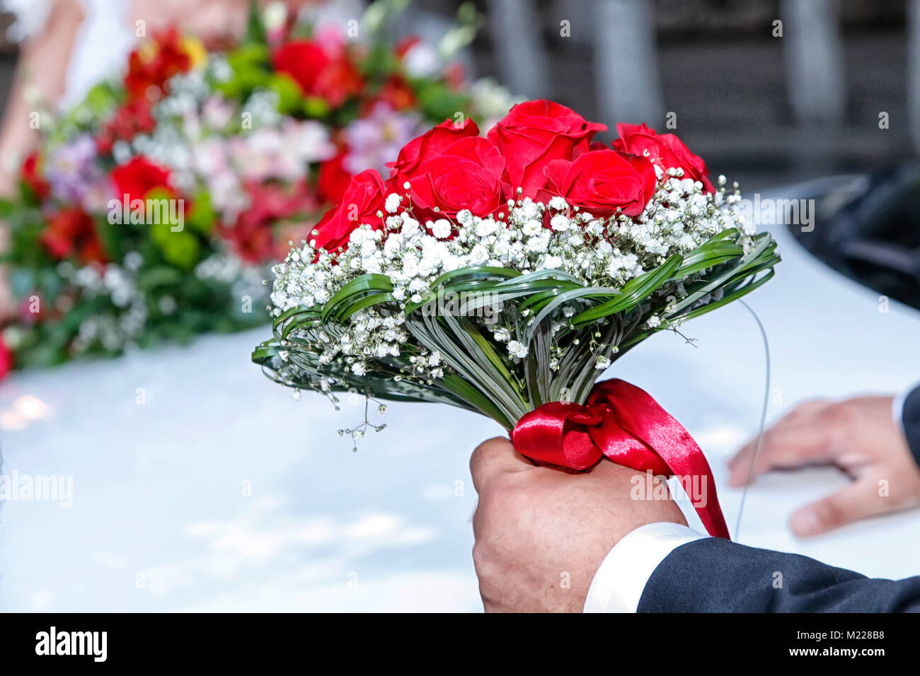 Elegante groom tenendo una gara rosa Bouquet nozze . Lo Sposo in un elegante vestito rosso che tiene nelle sue mani di nozze bouquet nuziale . Foto Stock