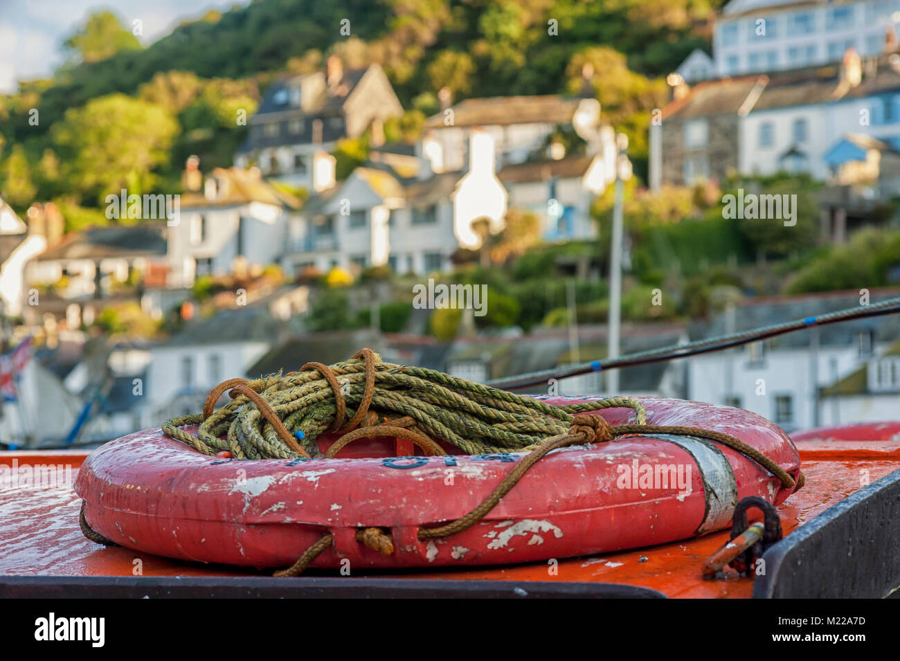 Cintura di salvataggio rossa sul peschereccio a strascico nel porto di Polperro con una vista sfocata del villaggio sullo sfondo Foto Stock