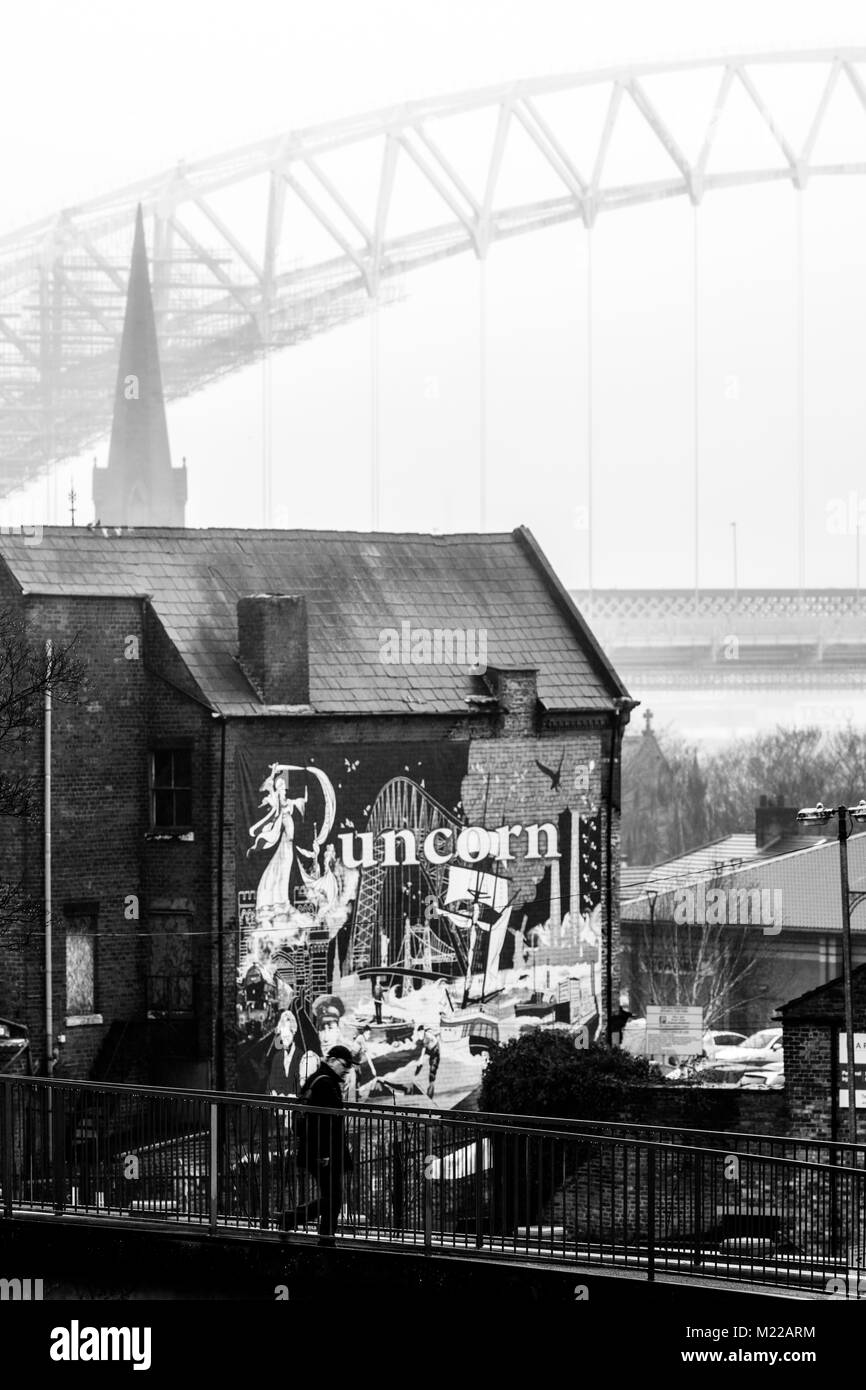 Una persona che cammina su un ponte di ferro attraverso la Bridgewater Canal nella città di Runcorn con murale di Runcorn e Silver Jubilee Bridge in background Foto Stock