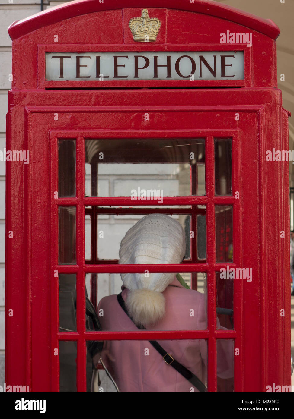 Una donna al telefono in una Londra casella telefono indossando un cappotto rosa e un bobble bat Foto Stock