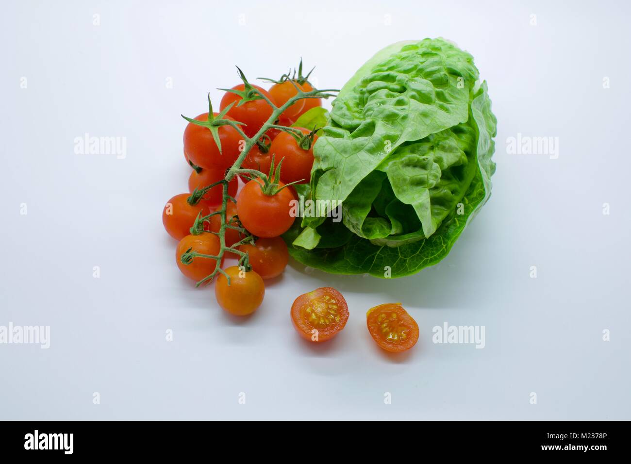 Pomodori ciliegia (Solanum Lycopersicum) accanto a un piccolo gioiello Lattughe (Lactuca sativa) su uno sfondo bianco Foto Stock