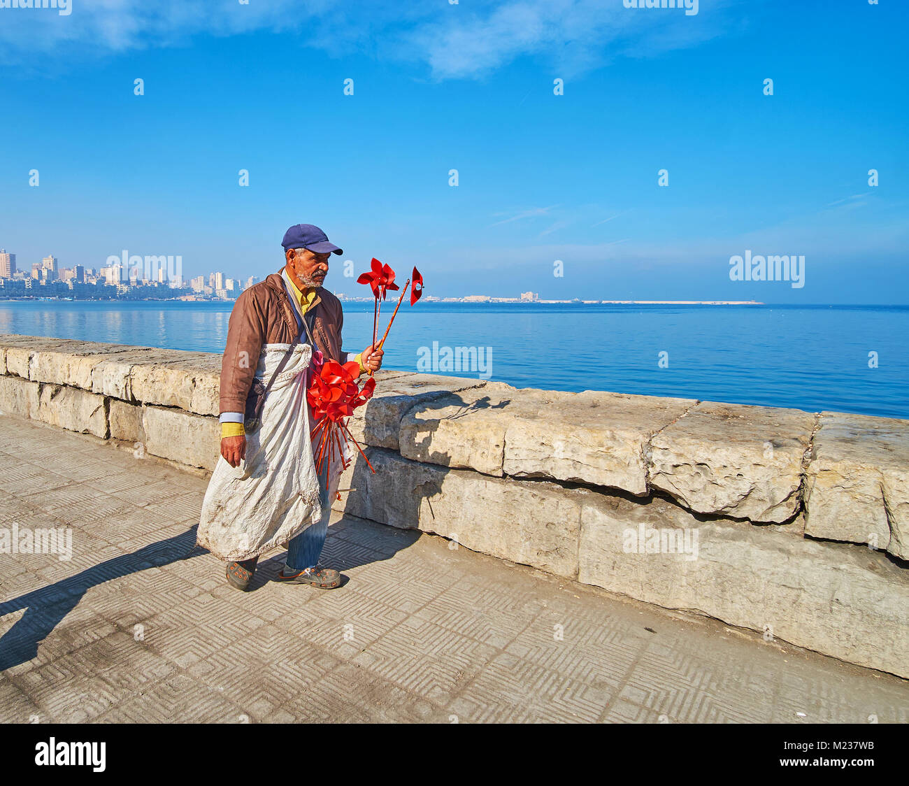 Alessandria, Egitto - 17 dicembre 2017: gli anziani fornitore con fiore rosso mulini a vento va lungo la Corniche promenade, il 17 dicembre ad Alessandria. Foto Stock