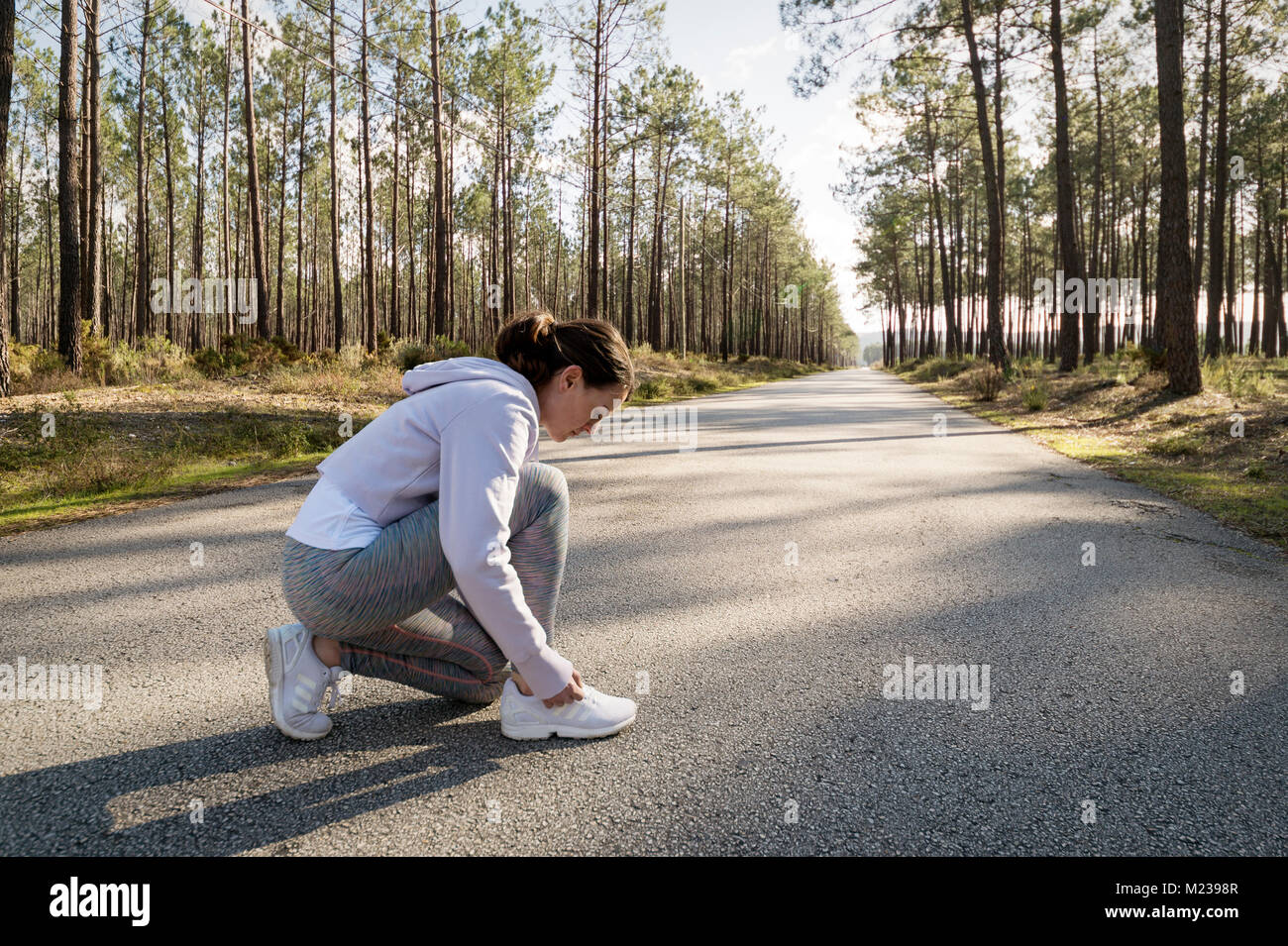 Runner donna facendo il suo lacci delle scarpe prima di fare jogging lungo una strada forestale. Foto Stock