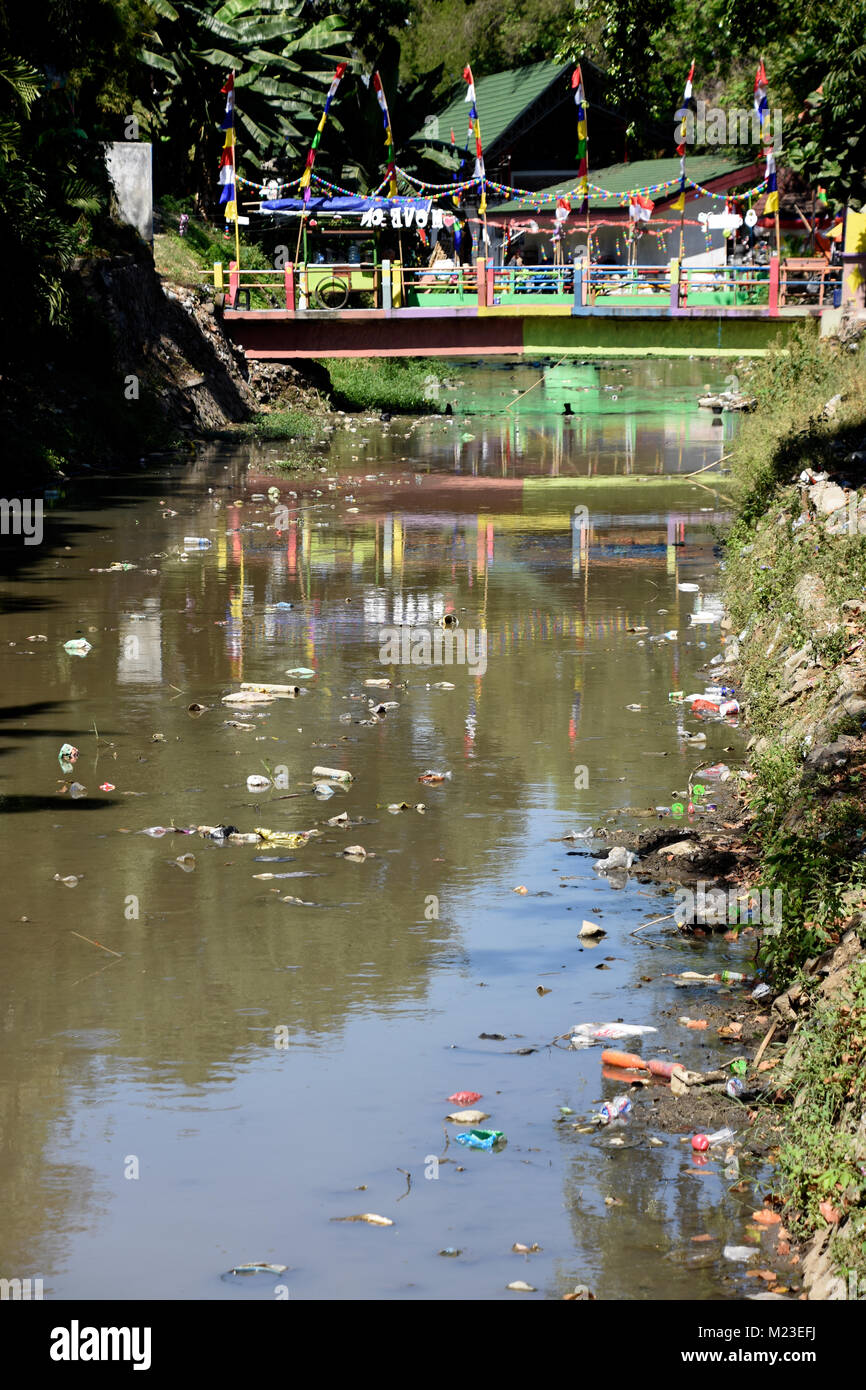 Spazzatura che scorre verso il basso un piccolo fiume in Indonesia, accanto a una delle baraccopoli zona denominata Villaggio verniciato Foto Stock
