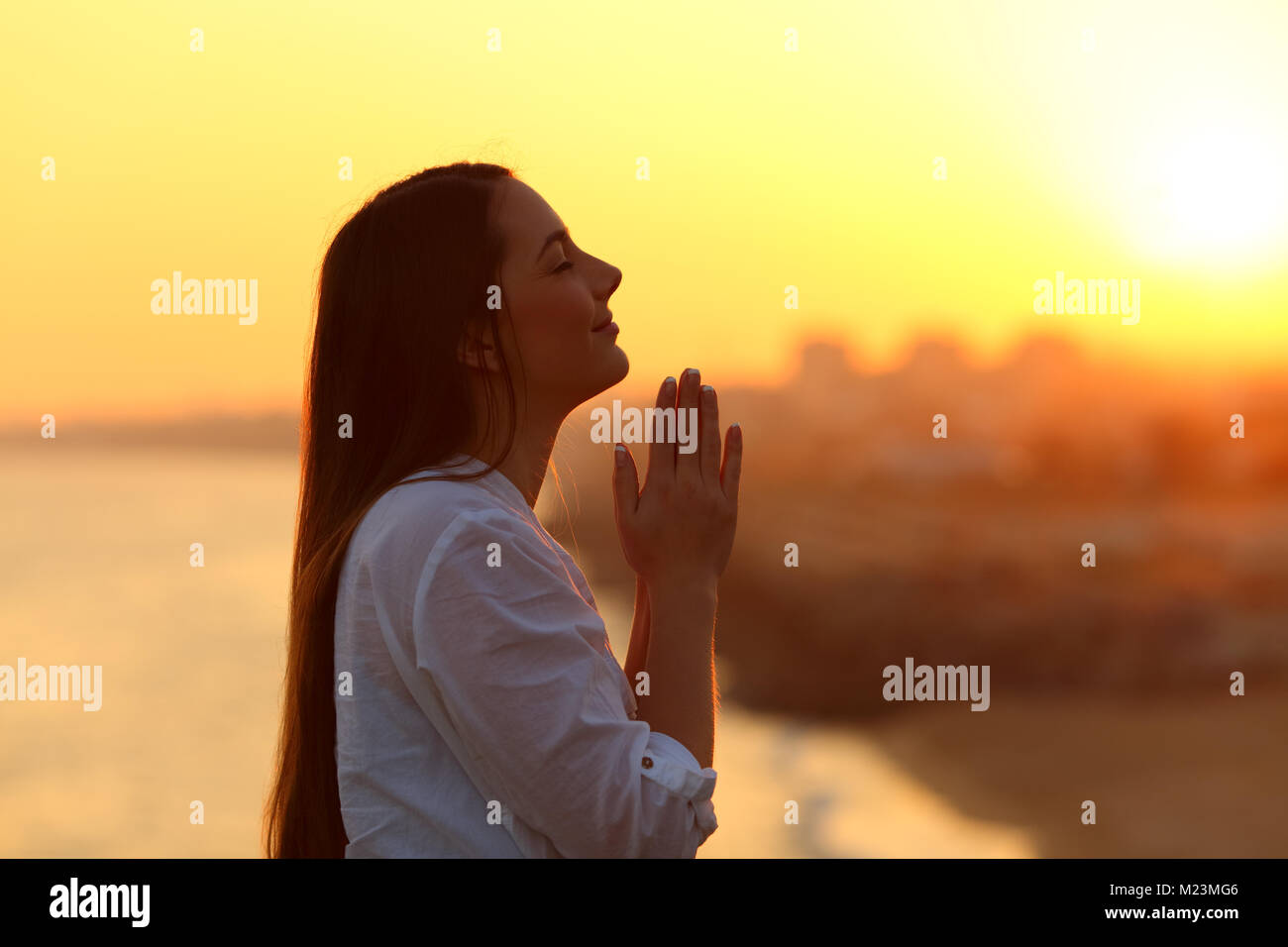 Vista laterale ritratto in controluce di una donna orante e guardando sopra al tramonto Foto Stock