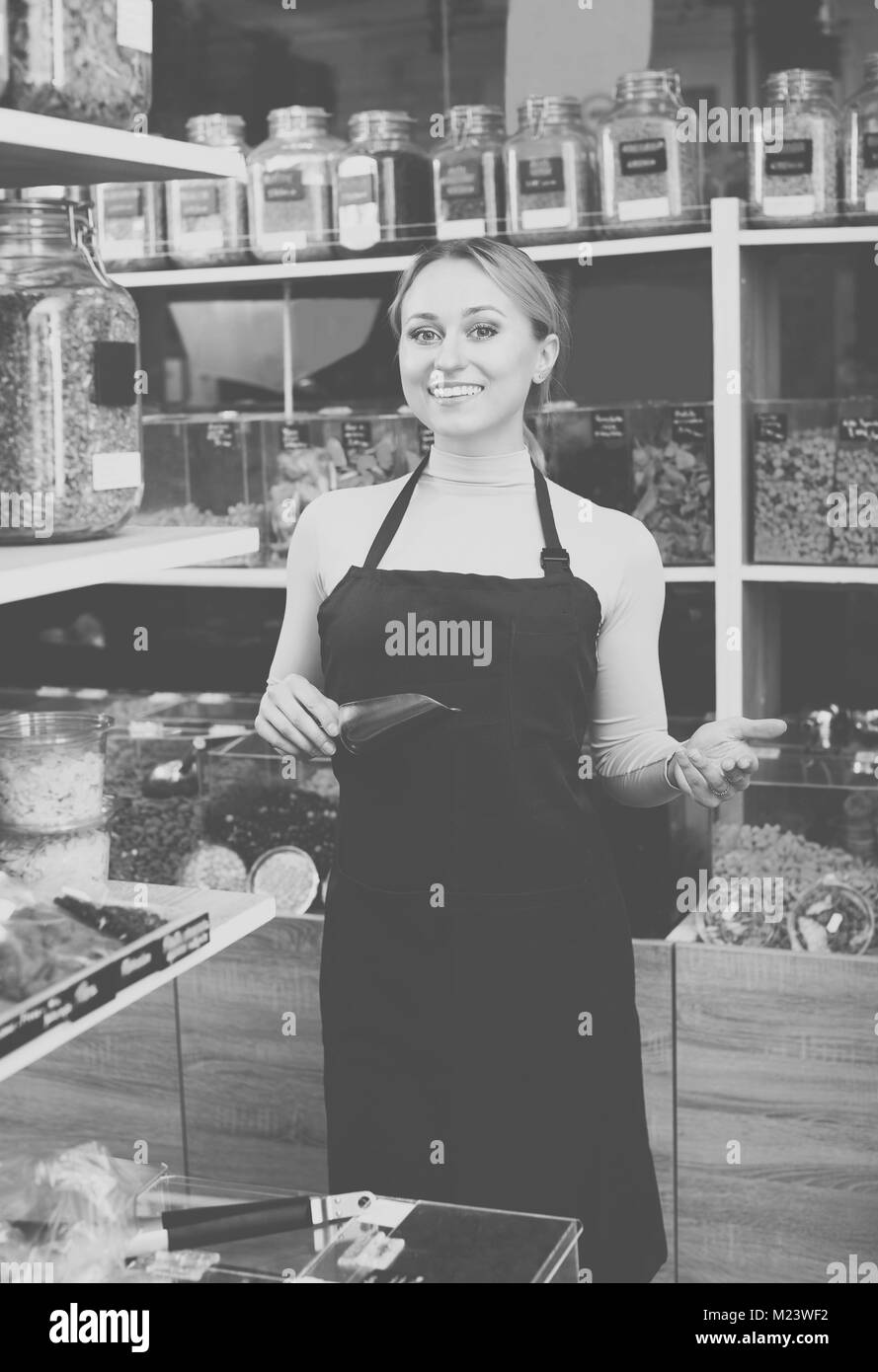 Sorridente giovane donna che indossa il grembiule e vendita di noci e frutta secca in organico negozio Foto Stock
