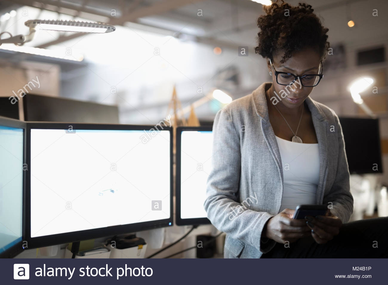 Imprenditrice dedicato utilizzando smart phone a computer in ufficio Foto Stock