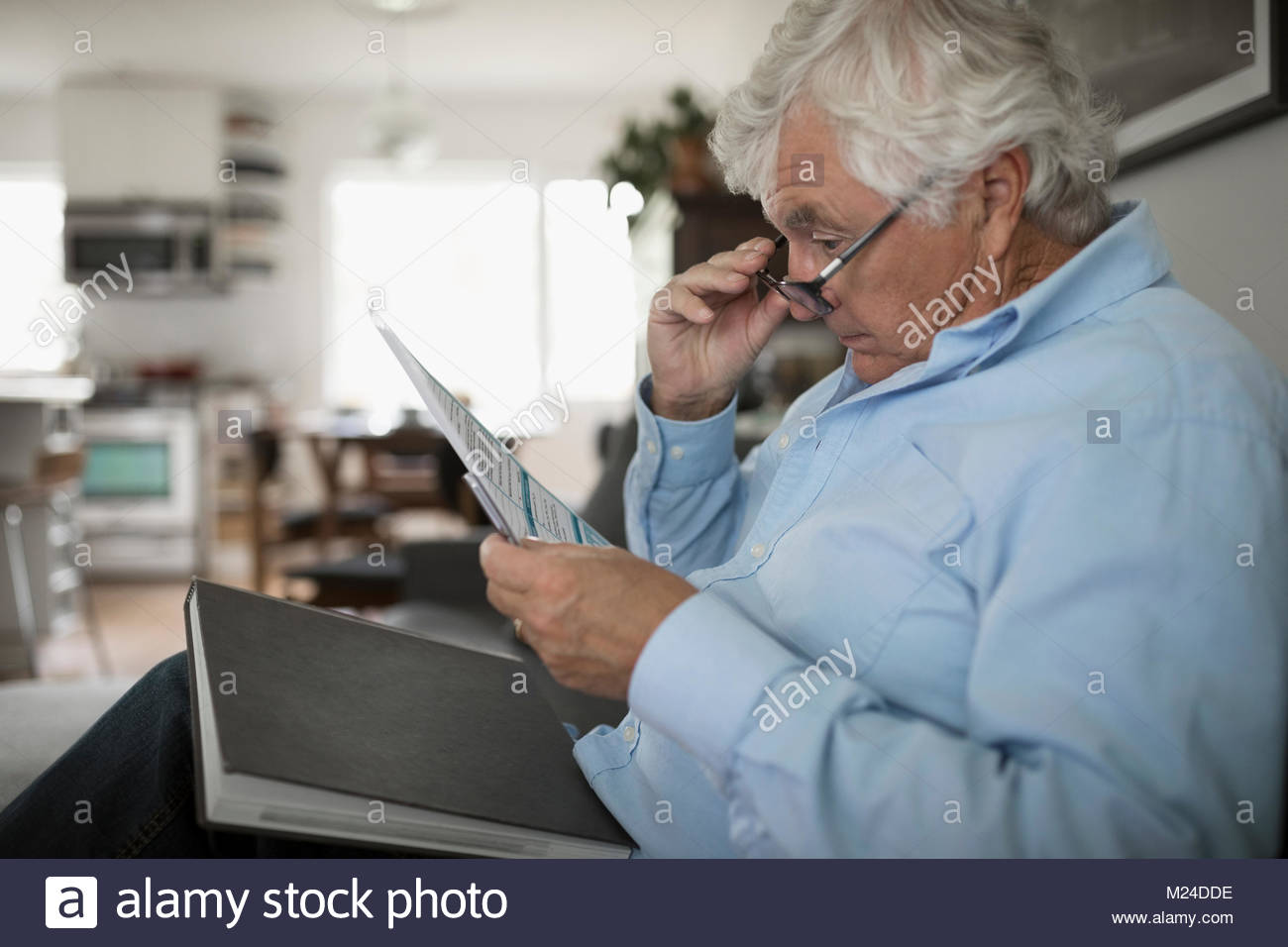 Senior di peering uomo al di là di occhiali in corrispondenza di documenti cartacei Foto Stock