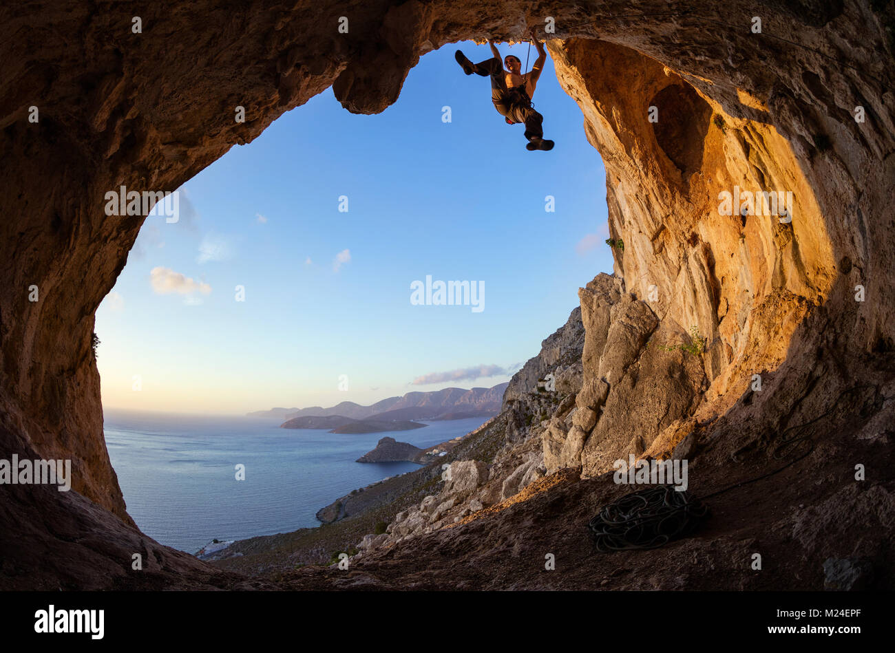 Giovane uomo portare arrampicata sul soffitto in grotta, appena prima del tramonto Foto Stock