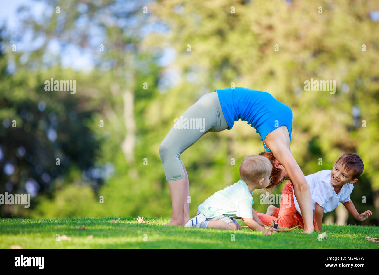 Giovane donna che lavora fuori in estate park, little figli giocando accanto a lei Foto Stock