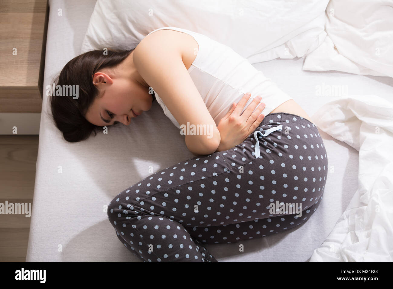 Vista in elevazione di una donna sdraiata sul letto di dolore allo stomaco Foto Stock