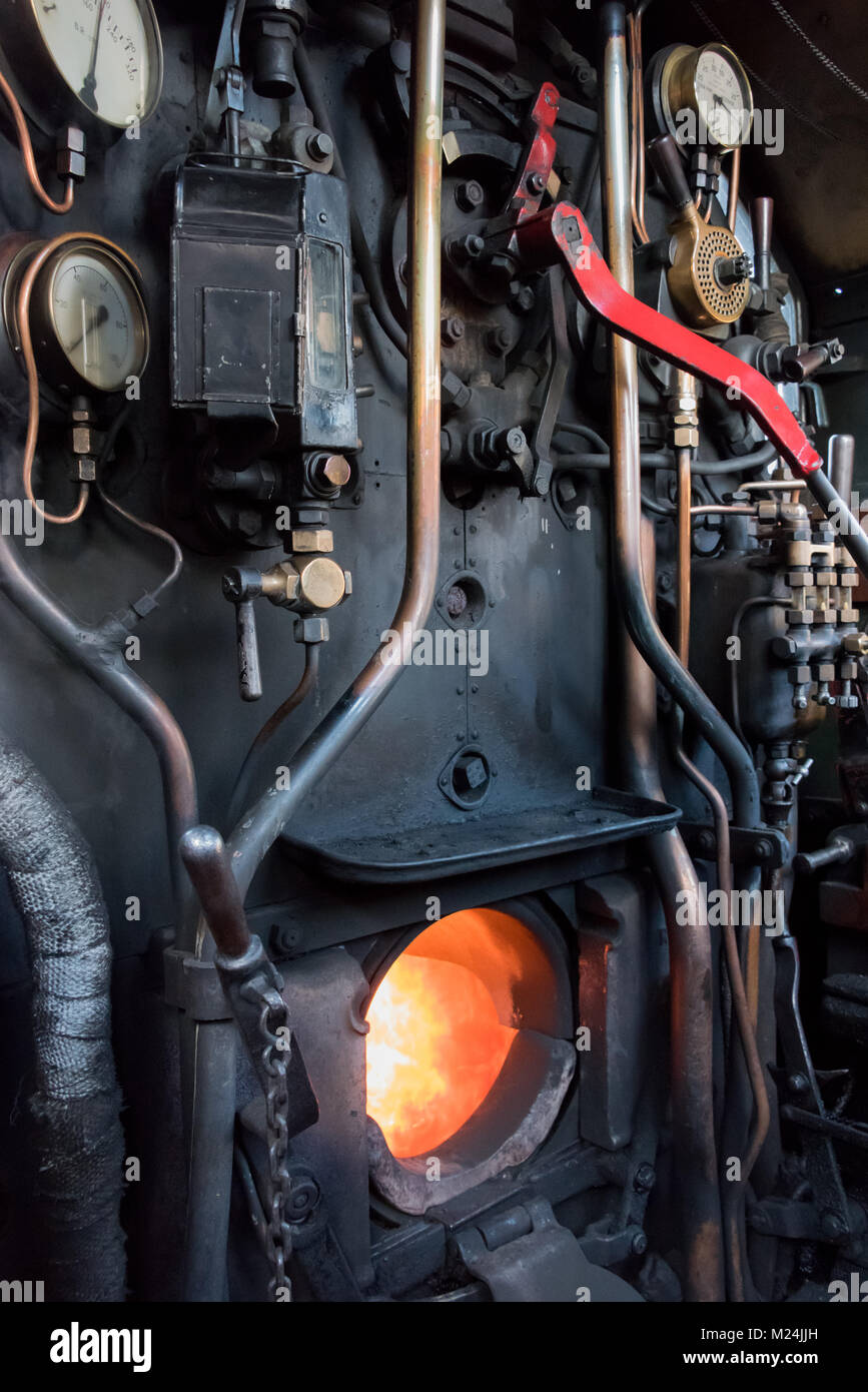 Formato verticale dell'interno dei comandi di guida su una vecchia locomotiva a vapore treno con la scatola di fuoco aperto che mostra le fiamme Foto Stock