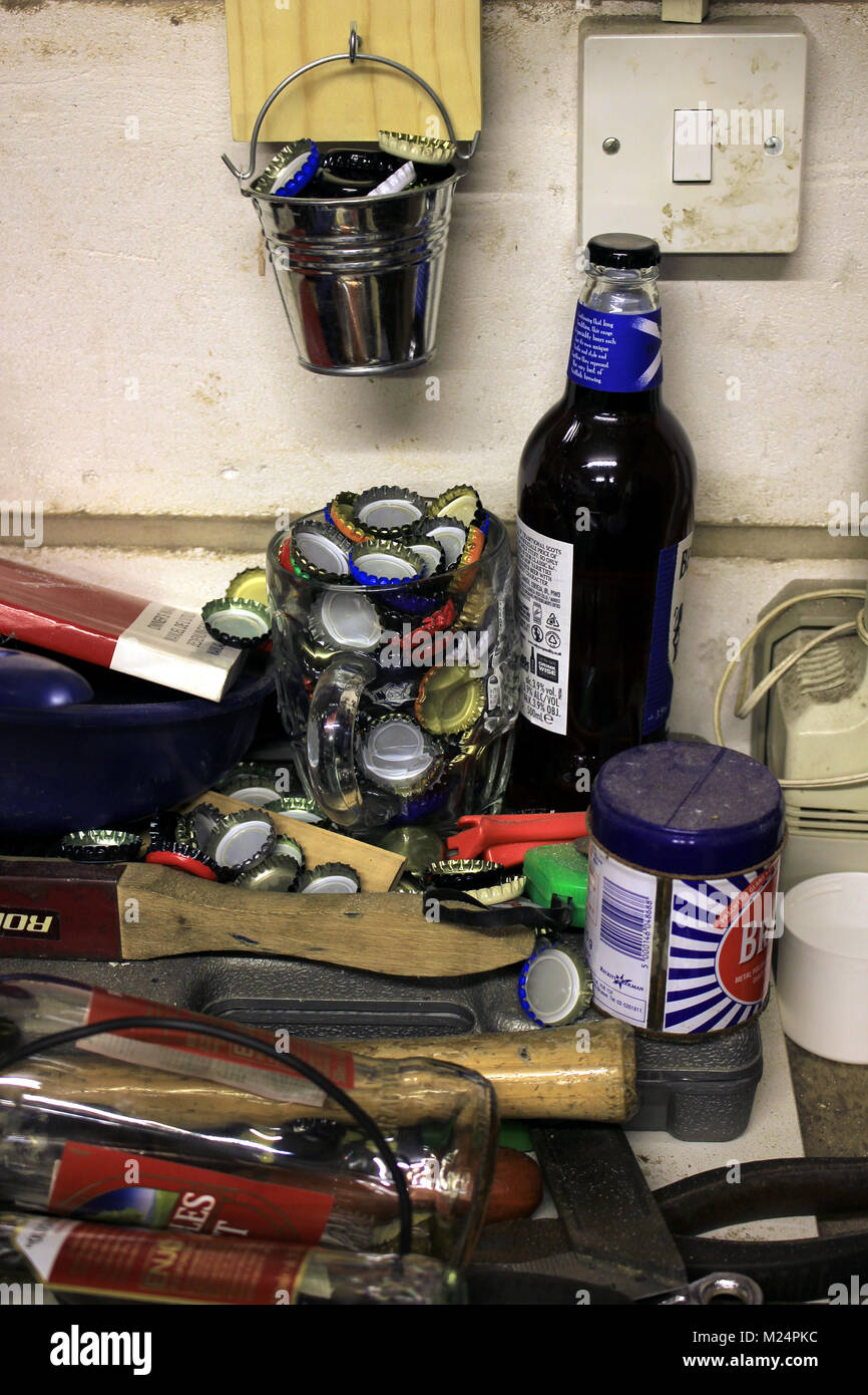 Bottiglie di birra e cime che hanno raccolto in una pinta di birra puntinati pot e hanno versato all'esterno tra gli strumenti su un banco in un workshop. Foto Stock