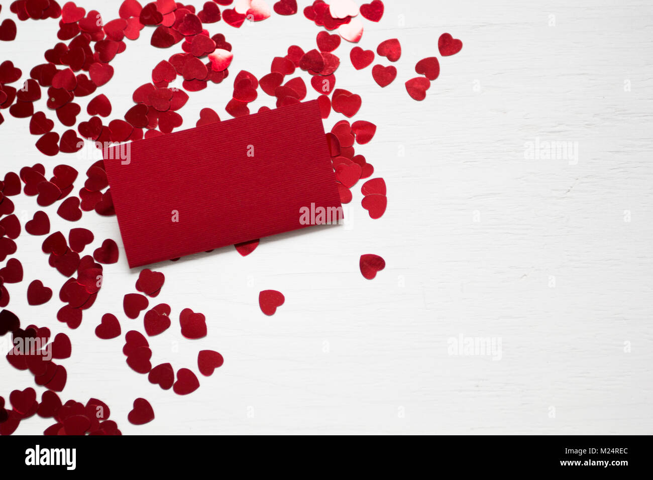 Il giorno di San Valentino del concetto. Cuori coriandoli e cartellino rosso su bianco tavolo in legno. Vista superiore Foto Stock