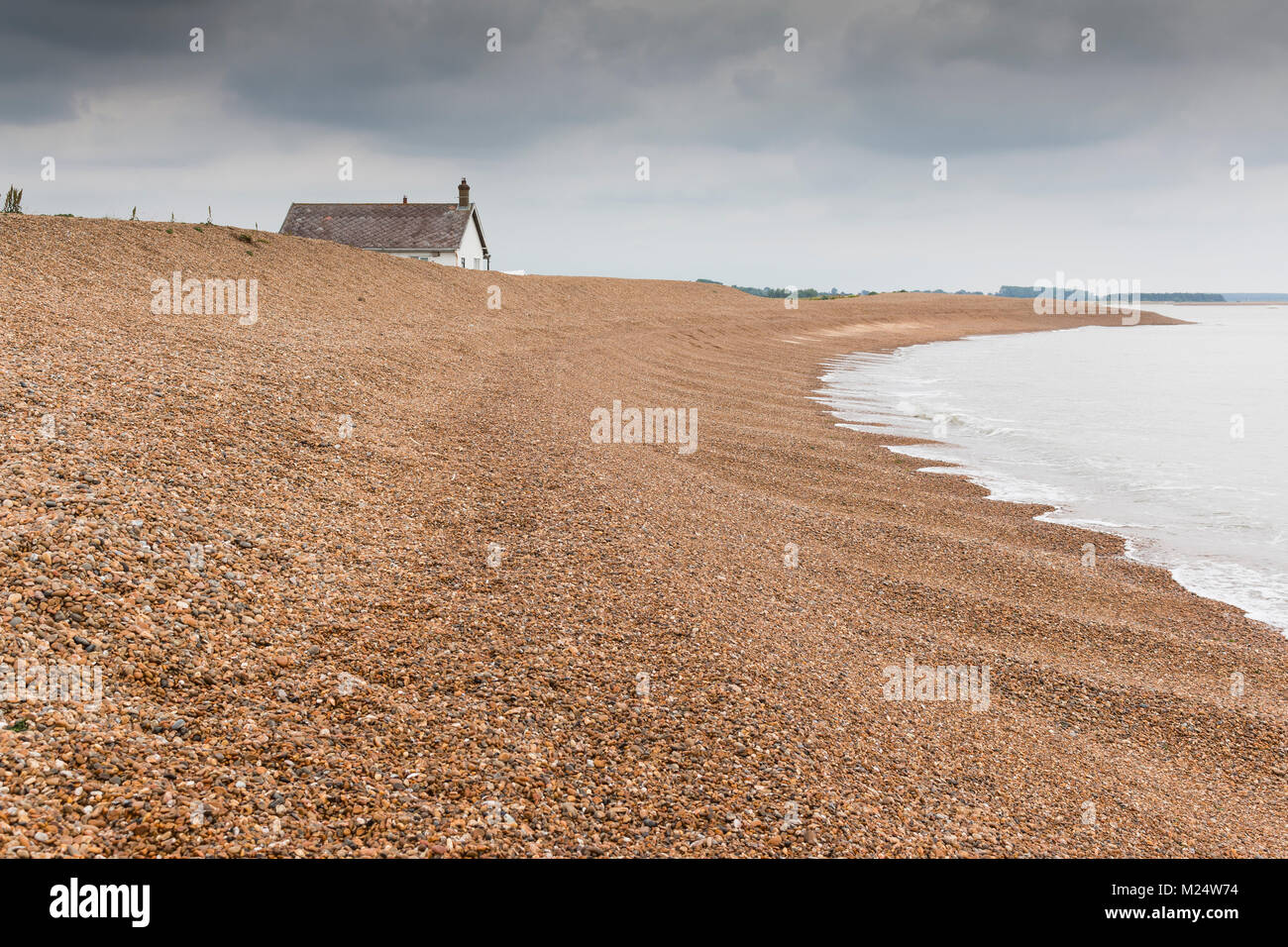 Una immagine di una solitaria casa al mare, mostrando una spiaggia di ciottoli con pendenza verso l'acqua a Shingle Street, Suffolk, Inghilterra, Regno Unito Foto Stock