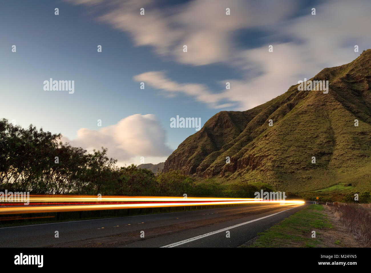 Sentieri di luce dalle vetture di guida lungo l'Autostrada 93 in Makaha Valley in Oahu, Hawaii Foto Stock