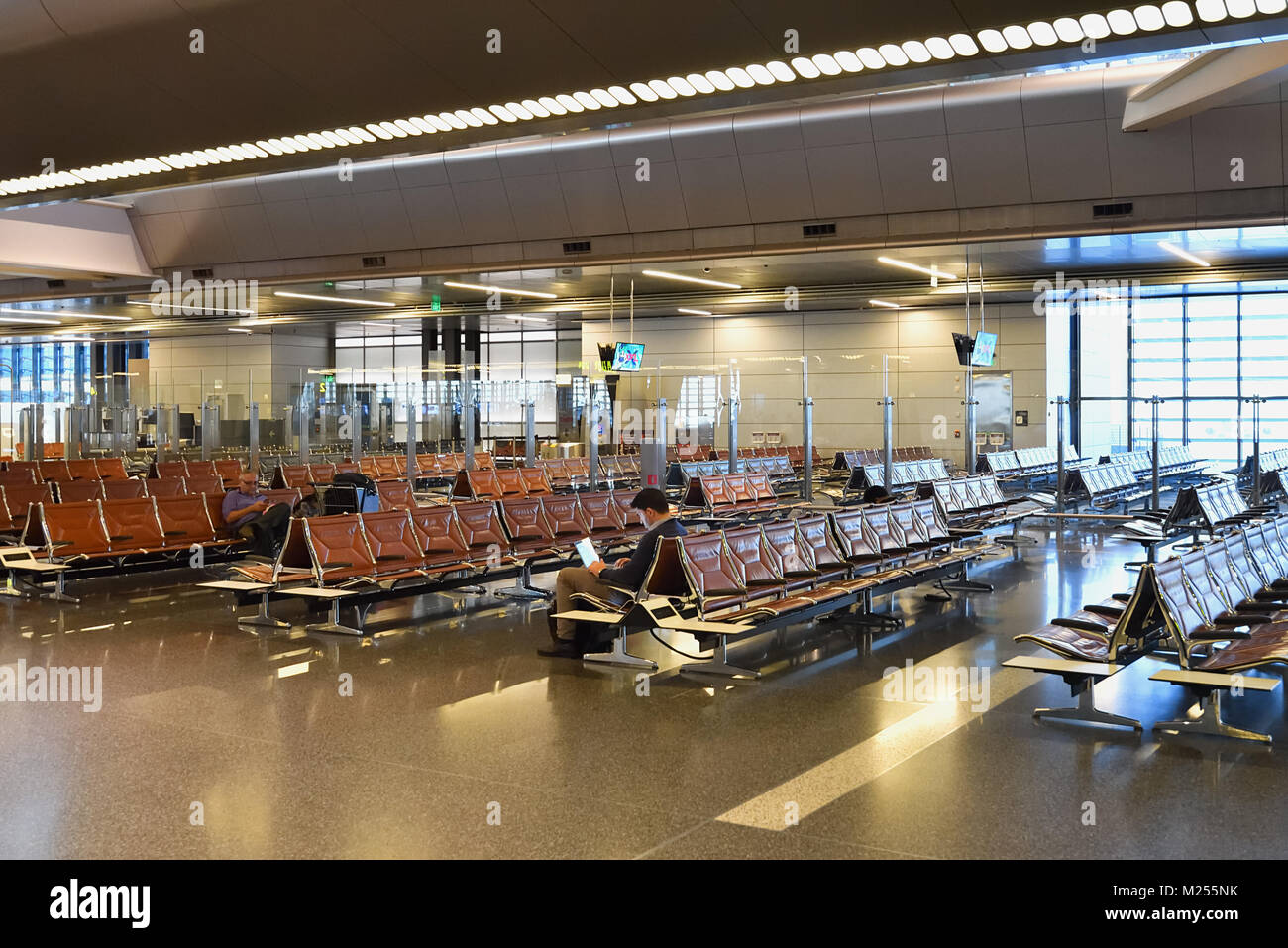 Il Qatar Doha, Hamad International Airport. Lungo i cancelli d'imbarco, un viaggiatore di affari continua a lavorare su un laptop mentre si attende per il suo volo. Foto Stock