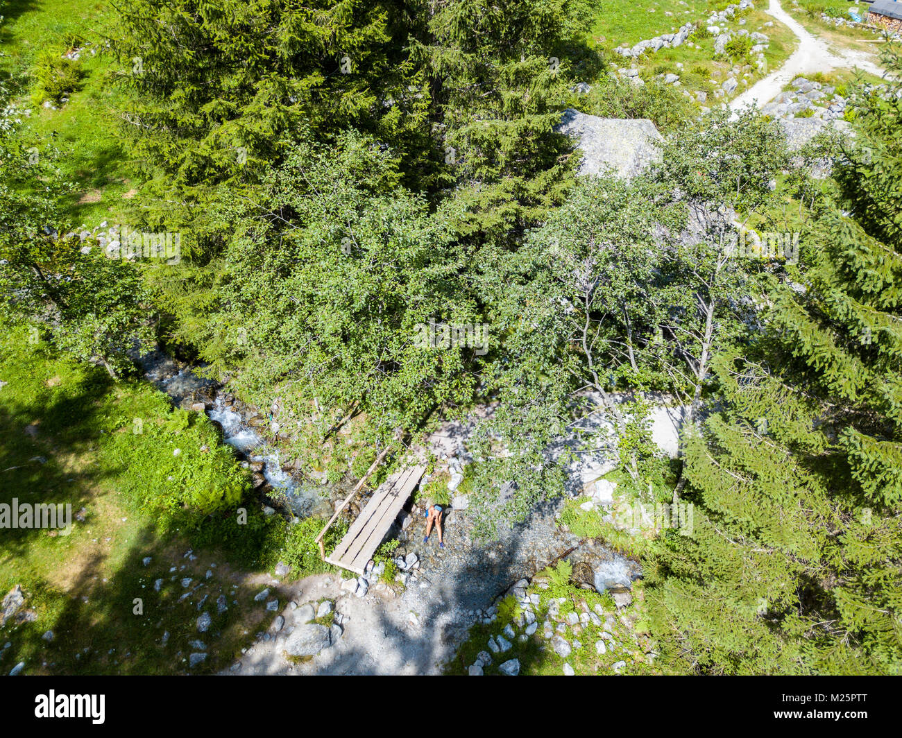 Vista aerea di un ponte di legno e un fiume in Val di Mello, una verde vallata circondata da montagne di granito e boschi. Italia Foto Stock
