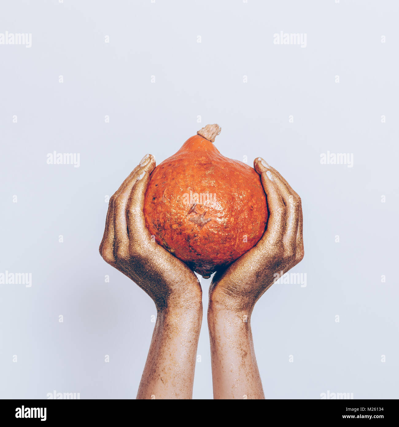 Mani femminili in oro dipingere tenendo una zucca arancione su sfondo blu Foto Stock