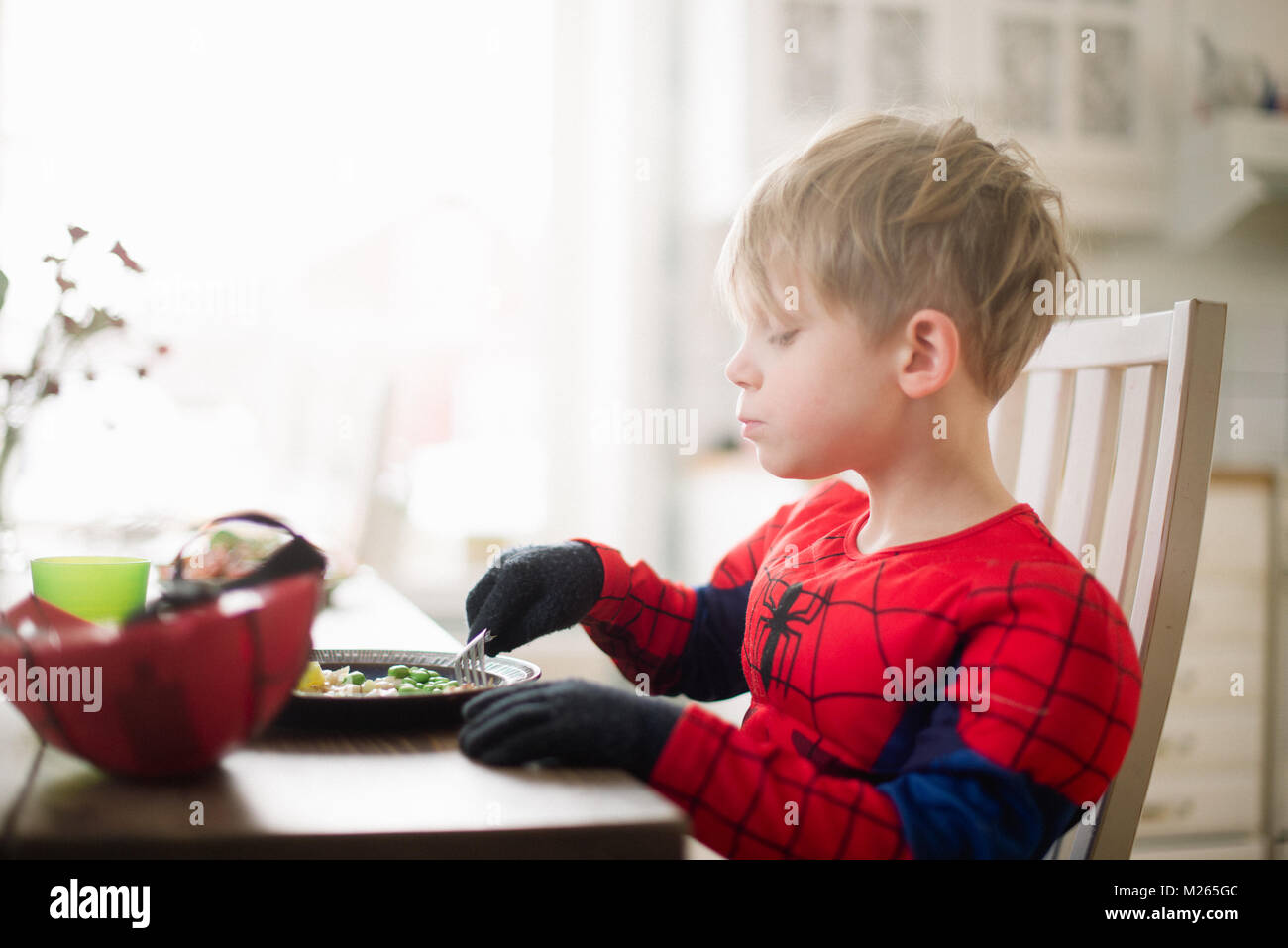 Boy scandinavo mangiare il suo pranzo in un uomo ragno costume. Foto Stock