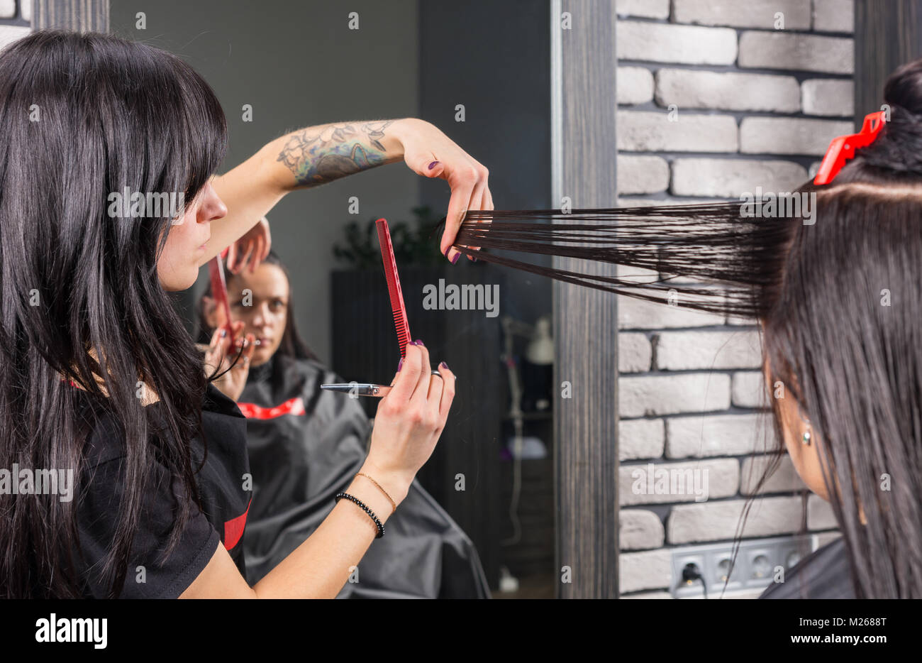 Femmina parrucchiere professionale il taglio e la modellazione marrone capelli da forbici e pettine di bruna giovane donna mentre è seduto in poltrona in bellezza Foto Stock