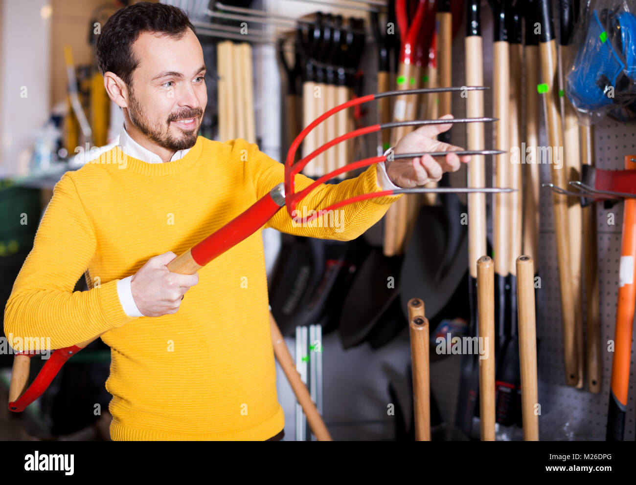 Felice il cliente maschio esaminando forche in garden equipment shop Foto Stock