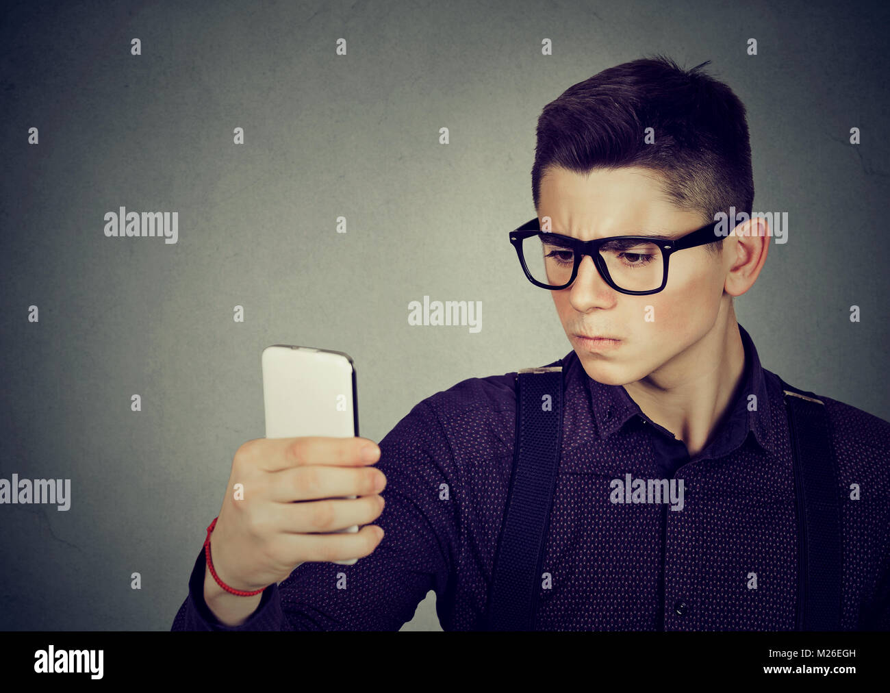Giovane uomo intelligente in occhiali accigliata tenendo selfie con lo smartphone. Foto Stock
