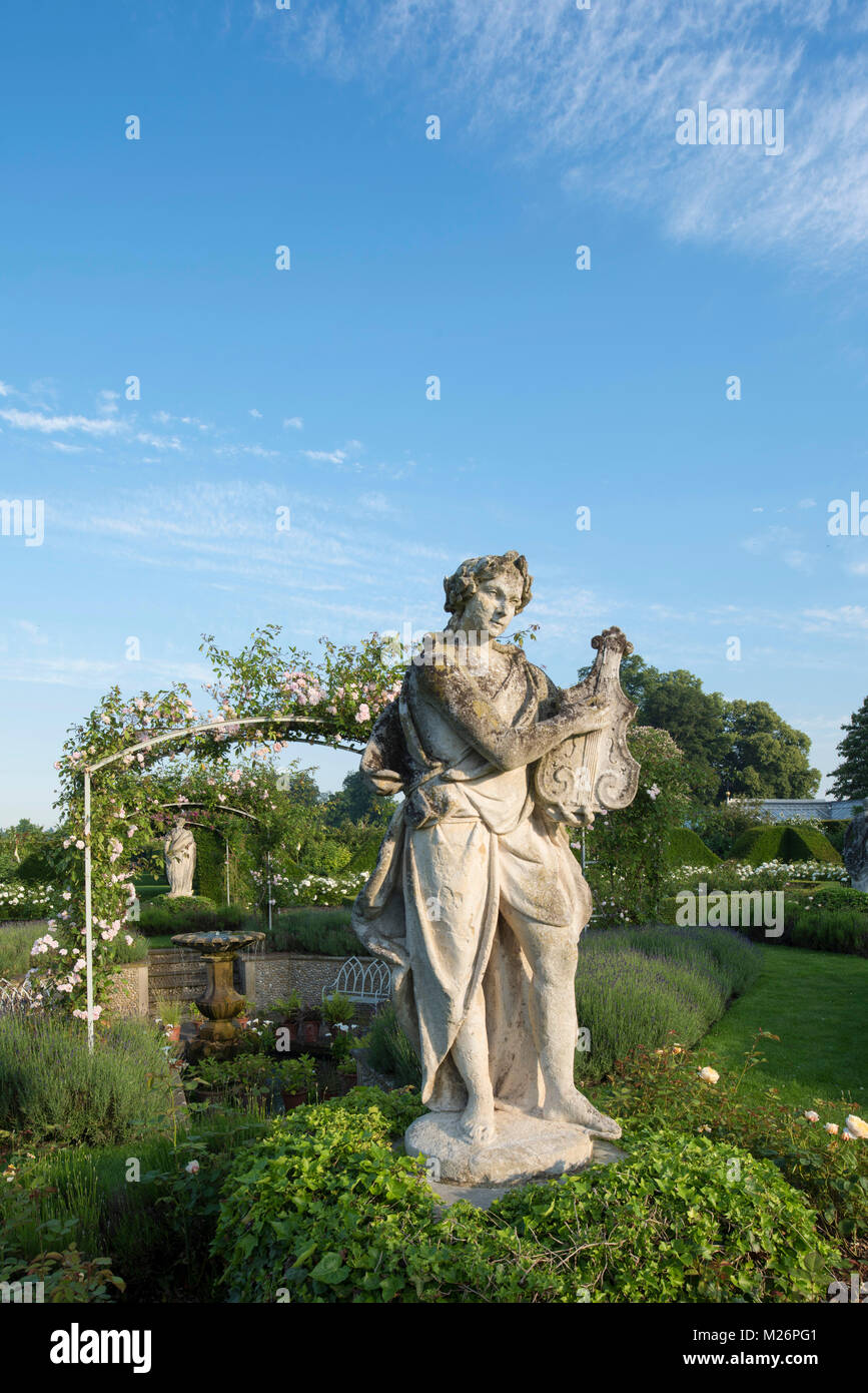 Una statua di pietra di un liuto giocatore nel parterre di rose nel giardino murato a Houghton Hall, King's Lynn, Norfolk, Regno Unito Foto Stock