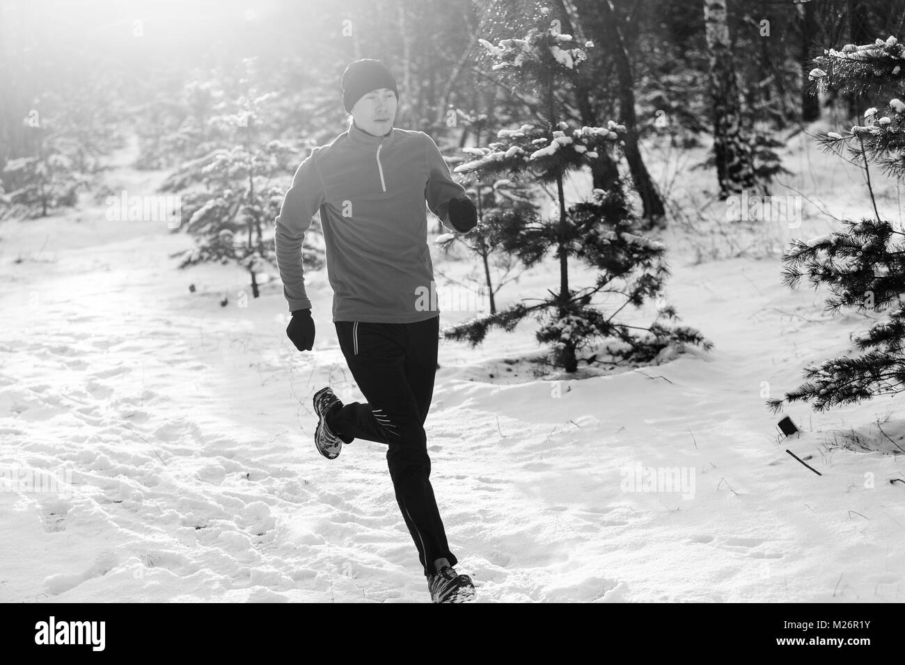 Foto in bianco e nero del giovane atleta che corre attraverso la foresta di inverno Foto Stock