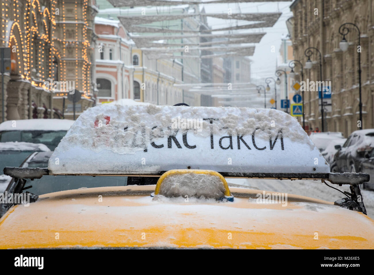 Yellow taxi con banner "Yandex taxi' su un tetto di una vettura in attesa per il passeggero in gomma negozio durante una nevicata a Mosca, Russia Foto Stock