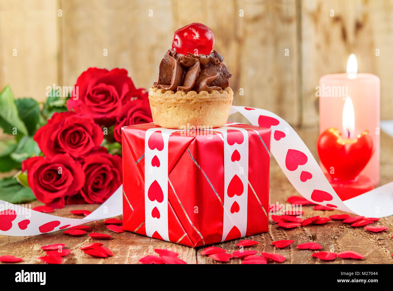 Tortina con la ciliegia sulla confezione regalo rossa nella parte anteriore del bouquet di rose rosse e candele su sfondo di legno. Il giorno di San Valentino del concetto. La festa della mamma concetto! Foto Stock