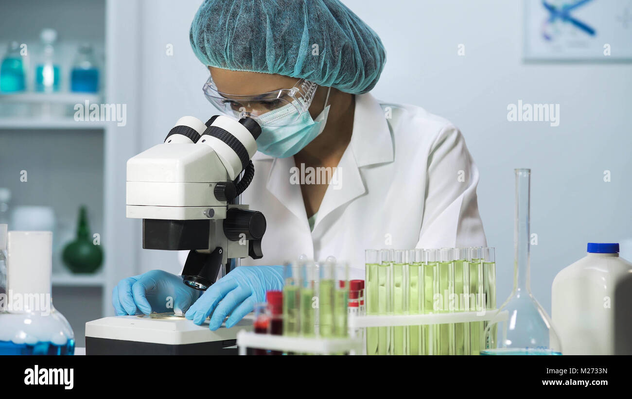 Donna scienziato che guarda nel microscopio, ricerche biochimiche, cosmetologia Foto Stock