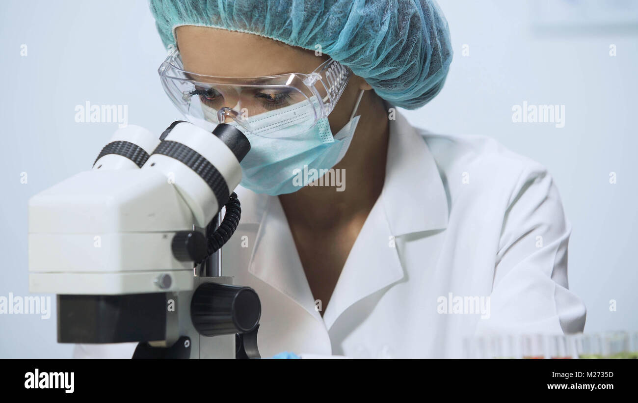 Razza mista medic cercando in microscopio, facendo ricerche biochimiche, close-up Foto Stock