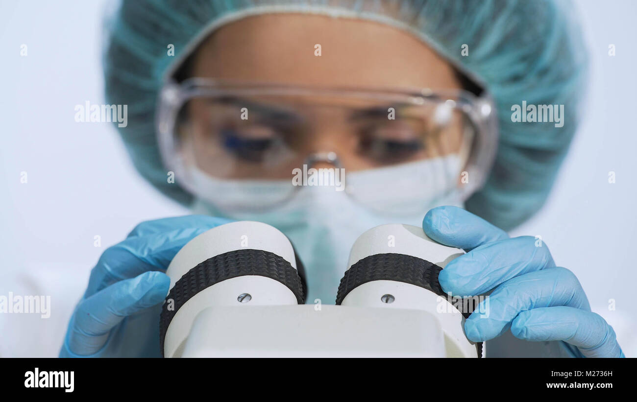 Razza mista donna che guarda nel microscopio, facendo ricerche biochimiche, primo piano Foto Stock