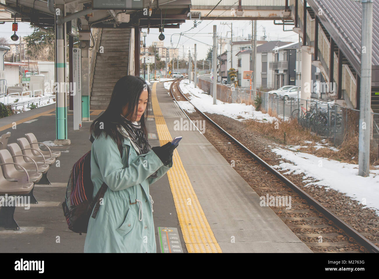 Viaggio vacanza invernale concetto : Ritratto donna asiatica traveler permanente sulla stazione ferroviaria e giocare il suo smartphone. Foto Stock