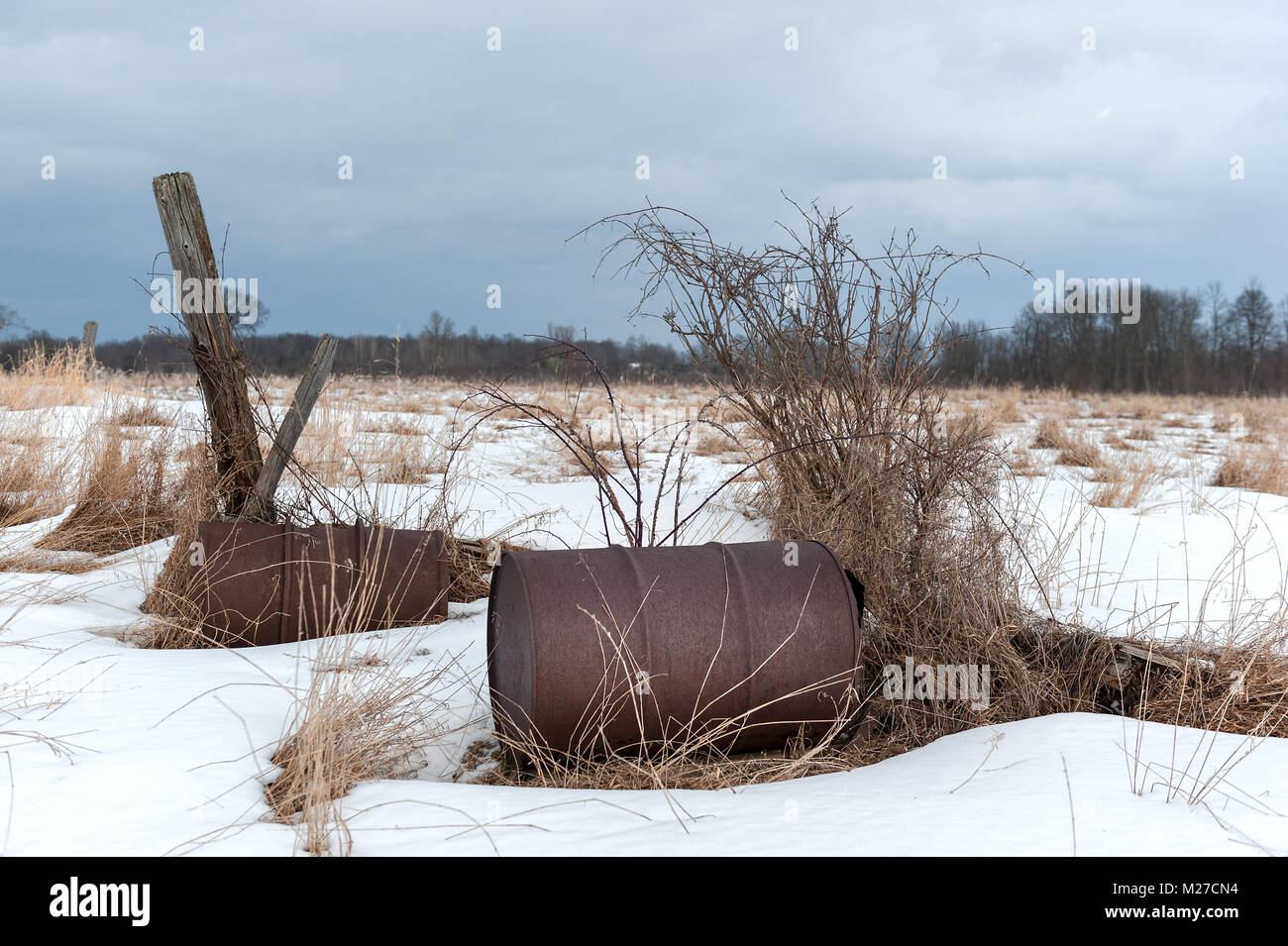 Arrugginimento abbandonate barili di olio in coperta di neve farm. Foto Stock